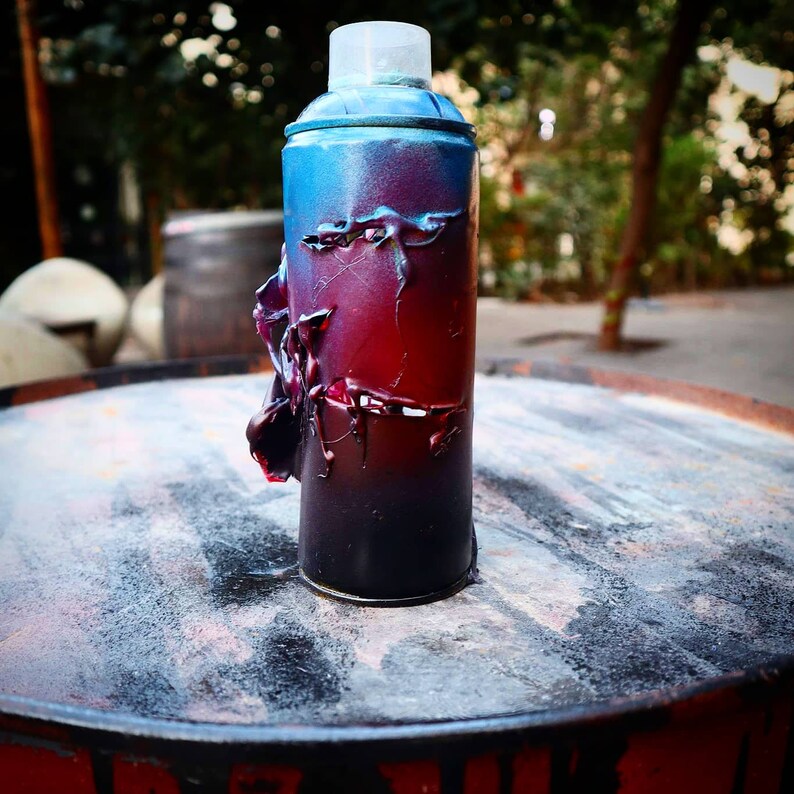 May include: A spray paint can with a blue, red, and black gradient. The can is covered in a layer of dried paint, giving it a textured appearance.