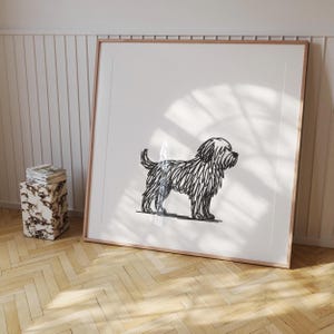May include: A framed art print featuring a black and white line drawing of a shaggy dog. The artwork is displayed in a light wood frame, leaning against a white wall. The dog is depicted in a side profile, with a fluffy coat and tail.