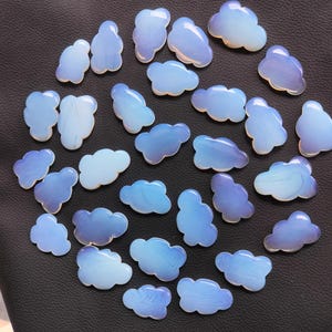 May include: A collection of 28 iridescent blue and white cloud-shaped cabochons. The cabochons are smooth and polished, with a variety of sizes and shapes.