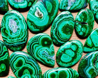 May include: A collection of green malachite cabochons with intricate patterns. The stones are smooth and polished, with a variety of shapes and sizes.