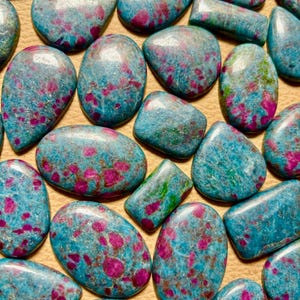 May include: A collection of blue and pink ruby zoisite cabochons. The stones are smooth and polished, with a variety of shapes and sizes.