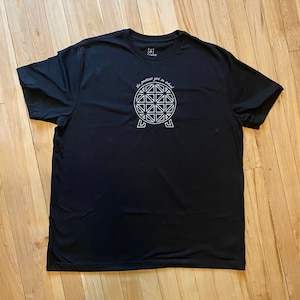 Pu&ograve; includere: Maglietta nera con una grafica bianca di una sfera con un motivo geometrico e il testo "the timeless gift to cherish".