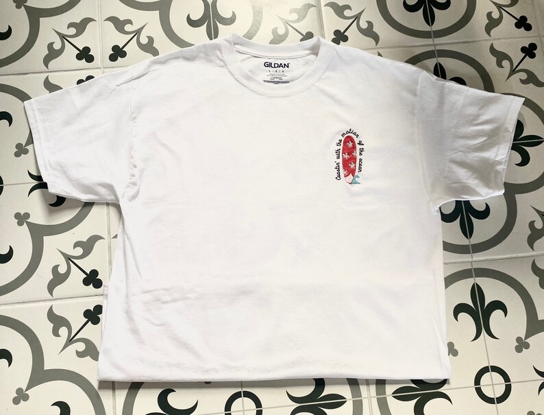 May include: White t-shirt with a red and white surfboard graphic and the text "Cruisin' with the motion of the ocean".