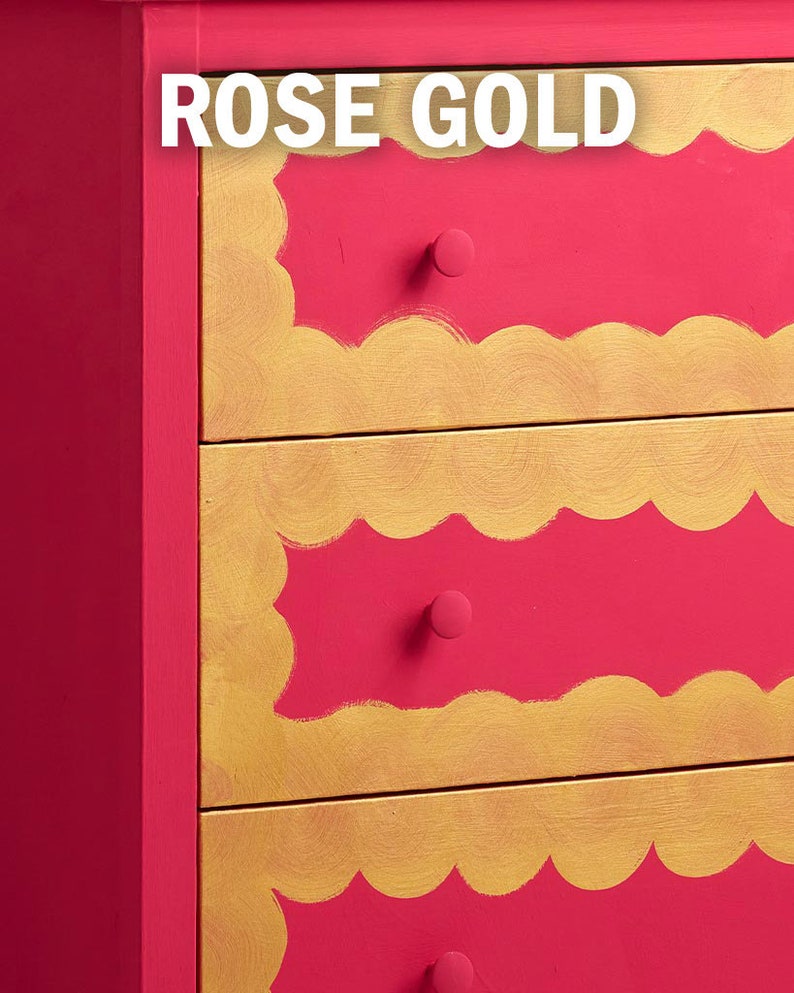 May include: A red dresser with gold trim and scalloped edges. The dresser has three drawers with gold knobs. The text "ROSE GOLD" is written in white on the top of the dresser.