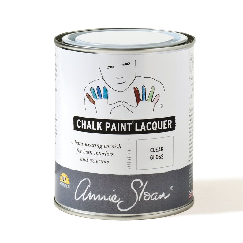 May include: A white can of Annie Sloan Chalk Paint Lacquer in clear gloss. The can has a hand-painted design of a person with colorful fingertips. The text on the can reads "Chalk Paint Lacquer", "a hard-wearing varnish for both interiors and exteriors", "Clear Gloss", and "UV Protection".