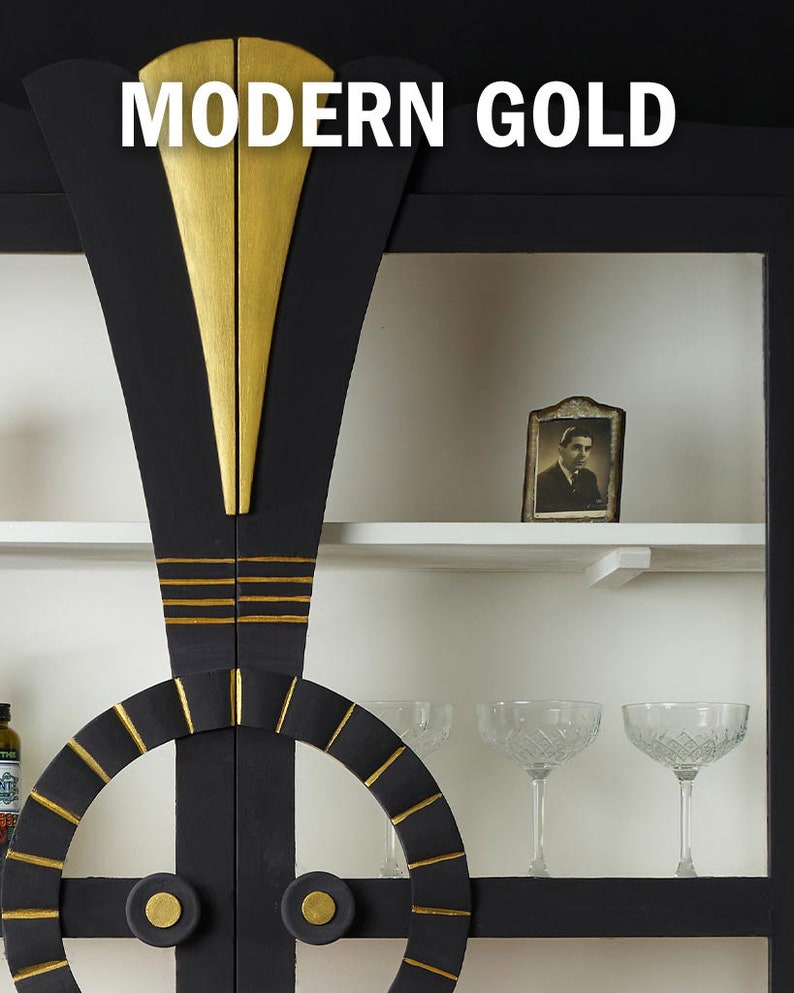 May include: A black cabinet with gold accents. The cabinet has two doors with a circular design and a gold trim. The doors are closed. The cabinet has shelves with a white background. There is a small framed photo on the top shelf. The cabinet is labeled "MODERN GOLD".