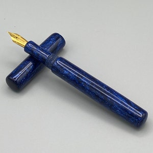 Puede incluir: Una pluma estilogr&aacute;fica azul y dorada con un dise&ntilde;o de m&aacute;rmol. La pluma est&aacute; cerrada y la tapa est&aacute; en el cuerpo.