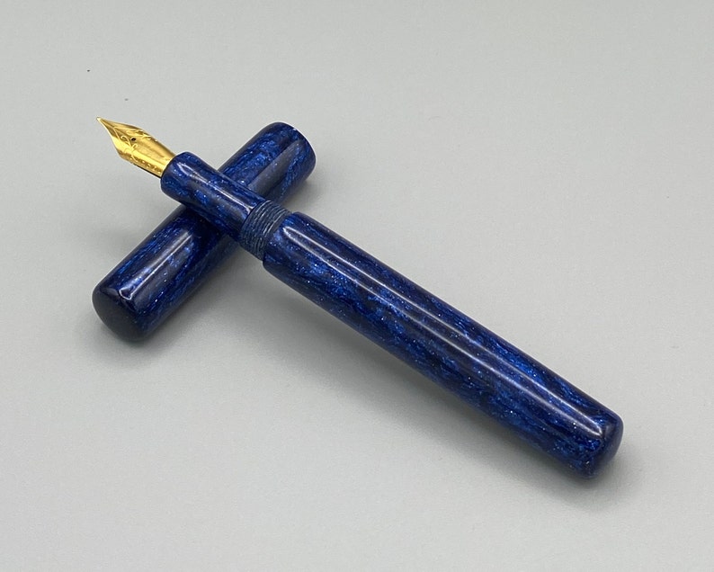 Puede incluir: Una pluma estilogr&aacute;fica azul y dorada con un dise&ntilde;o de m&aacute;rmol. La pluma est&aacute; cerrada y la tapa est&aacute; en el cuerpo.