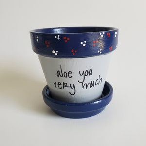 May include: A blue and white ceramic planter with red polka dots. The planter has the words "aloe you very much" written on it.