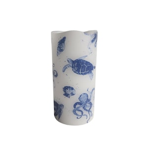 Könnte beinhalten: Weiße Kerze in Säulenform mit einem blauen und weißen Meereslebewesen-Design. Das Design zeigt einen Oktopus, eine Meeresschildkröte und Muscheln.