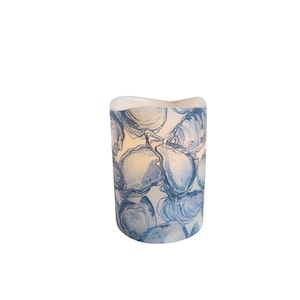 May include: A white pillar candle with a blue and white oyster shell pattern. The candle is lit and has a warm glow.