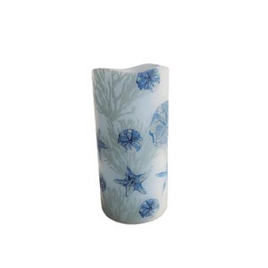 May include: A white pillar candle with a blue and gray seashell and starfish design.