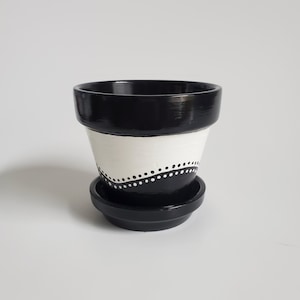May include: Black and white terracotta planter with a white band and a black dotted line design. The planter has a matching saucer.