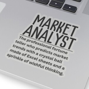 May include: A white laptop with a black sticker that says "MARKET ANALYST" and a definition of the term. The definition reads: "The professional fortune teller who predicts market trends with a crystal ball made of Excel sheets and a sprinkle of wishful thinking."