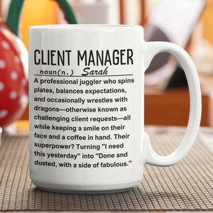Può includere: Una tazza da caffè in ceramica bianca con un design in bianco e nero che dice "CLIENT MANAGER noun(n.) Sarah A professional juggler who spins plates, balances expectations, and occasionally wrestles with dragons-otherwise known as challenging client requests-all while keeping a smile on their face and a coffee in hand. Their superpower? Turning "I need this yesterday" into "Done and dusted, with a side of fabulous."