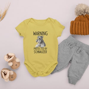 May include: Yellow baby onesie with a black and white image of a miniature schnauzer and the text "WARNING PROTECTED BY SCHNAUZER".