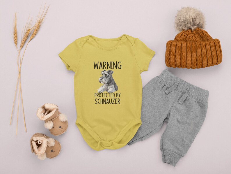 May include: Yellow baby onesie with a black and white image of a miniature schnauzer and the text "WARNING PROTECTED BY SCHNAUZER".