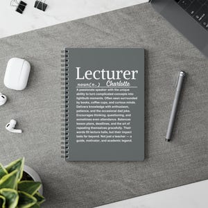 Könnte beinhalten: Ein graues Spiralnotizbuch mit dem Wort "Lecturer" in Weiß. Der Text unten beschreibt die Eigenschaften eines Dozenten. Ein silberner Stift, schwarze Büroklammern und kabellose Ohrhörer sind ebenfalls sichtbar.