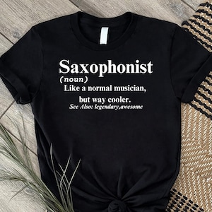 Könnte beinhalten: Ein schwarzes Kurzarm-T-Shirt mit weißem Textaufdruck: Saxophonist (noun) Like a normal musician, but way cooler. See Also: legendary,awesome. Das T-Shirt hat einen Rundhalsausschnitt und besteht aus einfarbigem schwarzem Stoff mit weißer Schrift.