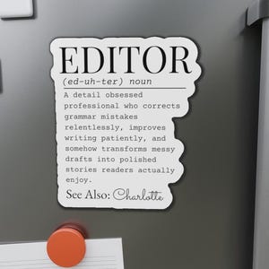 Peut inclure: Un aimant blanc avec la définition de "EDITOR" en texte noir. La définition décrit un éditeur comme un professionnel obsédé par les détails qui corrige les fautes de grammaire et transforme les brouillons désordonnés en histoires raffinées. Le texte "See Also: Charlotte" est également inclus.