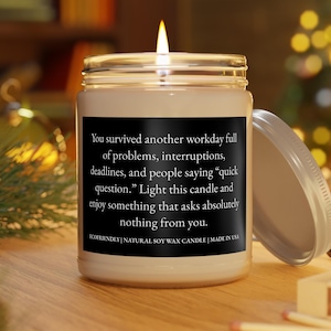 May include: A lit soy wax candle in a clear glass jar with a black label featuring white text that reads: You survived another workday full of problems, interruptions, deadlines, and people saying quick question. Light this candle and enjoy something that asks absolutely nothing from you. ECOFRIENDLY | NATURAL SOY WAX CANDLE | MADE IN USA.