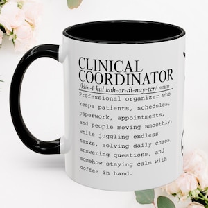 Könnte beinhalten: Ein weißer Keramikbecher mit schwarzem Henkel und schwarzem Innenrand. Der Becher ist mit schwarzem Text bedruckt, der einen klinischen Koordinator als professionellen Organisator definiert, der Patienten, Zeitpläne und Unterlagen verwaltet.