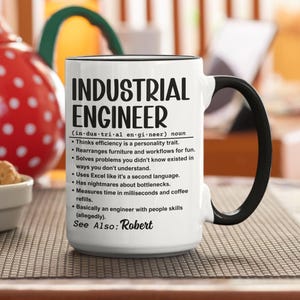 Puede incluir: Una taza de cerámica blanca con asa y borde negros. La taza presenta el texto "INDUSTRIAL ENGINEER" en letras negras grandes, junto con una definición y viñetas humorísticas sobre la profesión. También se incluye el texto "See Also: Robert".