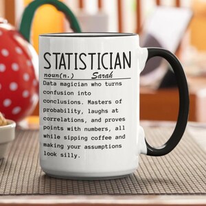 Può includere: Una tazza in ceramica bianca con manico e bordo neri, caratterizzata da un testo stampato in nero che definisce uno statistico come un mago dei dati che trasforma la confusione in conclusioni, padroneggia la probabilità e dimostra punti con i numeri.