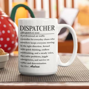Könnte beinhalten: Ein weißer Keramikbecher mit schwarzem Aufdruck, der das Wort DISPATCHER als professionellen Fluglotsen definiert, der Chaos bewältigt, Probleme löst und von Kaffee überlebt, mit dem Namen Andrea unter dem Punkt See Also.