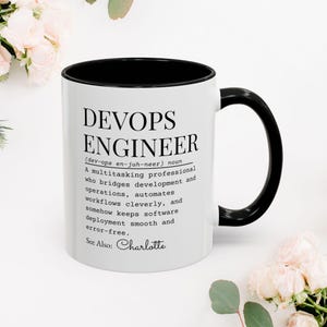 Puede incluir: Taza de cerámica blanca con interior y asa negros. La taza presenta el texto "DEVOPS ENGINEER" con una definición debajo. La definición describe a un profesional multitarea. Un gran regalo para un ingeniero de DevOps.