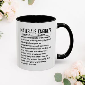 May include: White ceramic coffee mug with a black handle and rim. The mug has a black and white design that reads "MATERIALS ENGINEER noun(n.) Andrea Master mixologists of atoms and molecules, turning everyday stuff into superhero gear or indestructible couch cushions. They spend their days nerding out over polymers and ceramics, hoping their creations don't accidentally turn into slime or launch into space. Basically, they make sure your world stays together, literally."