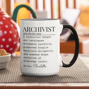 May include: White ceramic mug with a black handle and rim. The mug features the definition of "ARCHIVIST" in black text, including the pronunciation and a description of the role. The name "Charlotte" is also included.
