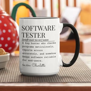 May include: White ceramic mug with black handle and rim. The mug features the text "SOFTWARE TESTER" and a definition. The mug also includes the name "Charlotte".
