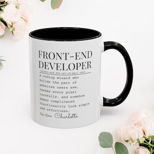 May include: White ceramic mug with a black interior and handle. The mug features the text "FRONT-END DEVELOPER" with a definition, and the name "Charlotte" at the bottom. The mug is surrounded by flowers.