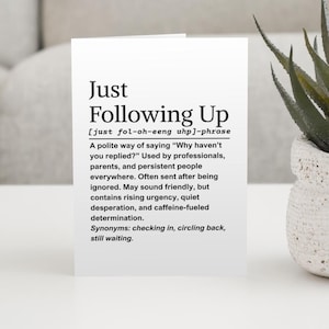 May include: A white card with the phrase "Just Following Up" in black, bold text. The card provides a definition, pronunciation, and synonyms for the phrase. A small potted plant is visible in the background.