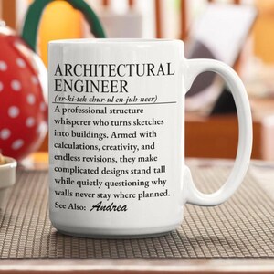 Puede incluir: Una taza de cerámica blanca con texto impreso en negro que define a un ingeniero arquitectónico como un susurrador de estructuras profesional que convierte bocetos en edificios, incluyendo el nombre Andrea bajo See Also.