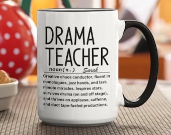 Może przedstawiać: Biały ceramiczny kubek z czarnym uchwytem i obramowaniem. Kubek zawiera tekst "DRAMA TEACHER" pogrubionymi czarnymi literami, wraz z definicją i dodatkowym tekstem. Idealny prezent dla nauczycieli dramatu.