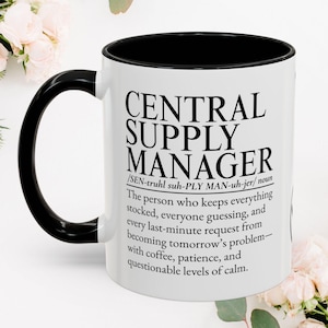 Op de afbeelding: Een witte keramische mok met een zwarte binnenkant en handvat. De buitenkant is voorzien van zwarte tekst: CENTRAL SUPPLY MANAGER /SEN-truhl suh-PLY MAN-uh-jer/ noun The person who keeps everything stocked, everyone guessing, and every last-minute request from becoming tomorrow’s problem—with coffee, patience, and questionable levels of calm.
