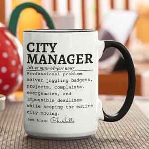 Può includere: Una tazza in ceramica bianca con manico e bordo neri, caratterizzata da un testo nero che definisce un City Manager come un risolutore di problemi professionale che gestisce budget, progetti, reclami, emergenze e scadenze impossibili. Include See Also: Charlotte.