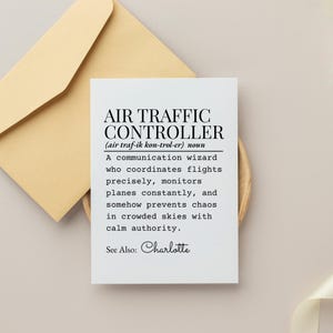 May include: A white card with the text "AIR TRAFFIC CONTROLLER" and a definition. The card is on a wooden surface with a tan envelope in the background. The text includes the name "Charlotte".