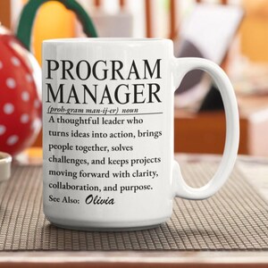 Op de afbeelding: Een witte keramische mok met zwarte tekst die de term Program Manager definieert als een doordachte leider die ideeën omzet in actie, uitdagingen oplost en projecten vooruit helpt met helderheid, samenwerking en doelgerichtheid. Zie ook: Olivia.