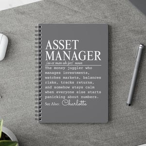 Pode incluir: Um caderno de espiral cinzento com texto branco que diz ASSET MANAGER, seguido de uma pronúncia fonética, uma definição que descreve um gestor de ativos e o texto See Also: Charlotte na parte inferior da capa.