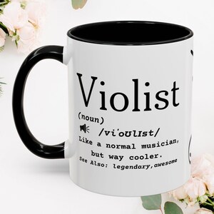 May include: A white ceramic mug with a black interior and handle. The front features black text that reads: Violist (noun) /vi'oulist/ Like a normal musician, but way cooler. See Also: legendary, awesome. A small speaker icon is printed above the text.
