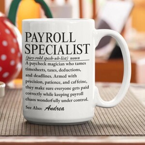 Peut inclure: Un mug en céramique blanche avec un texte imprimé en noir définissant un spécialiste de la paie comme un magicien des bulletins de salaire qui gère les feuilles de temps, les taxes, les déductions et les délais. Le texte se termine par See Also: Andrea.