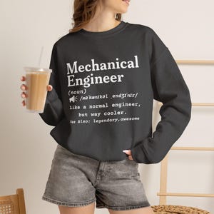 Peut inclure: Un sweat-shirt gris foncé à manches longues avec le texte blanc suivant : Mechanical Engineer (noun) /məˈkænɪkəl ˌɛndʒɪˈnɪr/ Like a normal engineer, but way cooler. See Also: legendary, awesome. Le sweat-shirt possède un col rond et des poignets côtelés.