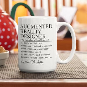 Può includere: Tazza in ceramica bianca con la scritta "AUGMENTED REALITY DESIGNER" in nero. La tazza include una definizione del termine e il nome "Charlotte". La tazza ha un manico grande ed è su una superficie a motivi.