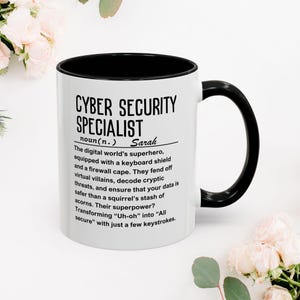 Könnte beinhalten: Weiße Keramik-Kaffeetasse mit schwarzem Rand und Henkel. Die Tasse zeigt eine schwarz-weiße Grafik mit dem Text "Cyber Security Specialist" und einer Definition des Begriffs. Der Name "Sarah" ist in der Definition enthalten.