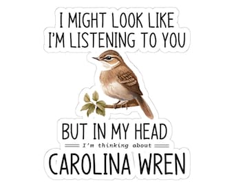 May include: A sticker with the text "I MIGHT LOOK LIKE I'M LISTENING TO YOU BUT IN MY HEAD I'm thinking about CAROLINA WREN." The sticker features a watercolor illustration of a Carolina Wren bird perched on a branch.