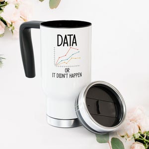 以下が含まれることがあります： 黒いハンドルと蓋が付いた白いトラベルマグ。マグには、グラフのイラストの上に「DATA」という文字と、その下に「OR IT DIDN'T HAPPEN」というフレーズが描かれています。蓋はシルバーと黒です。