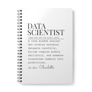 以下が含まれることがあります： 「DATA SCIENTIST」の黒い文字が書かれた白いリング綴じノート。データサイエンティストの定義が書かれています。「See Also: Charlotte」の文字がページの下部にあります。